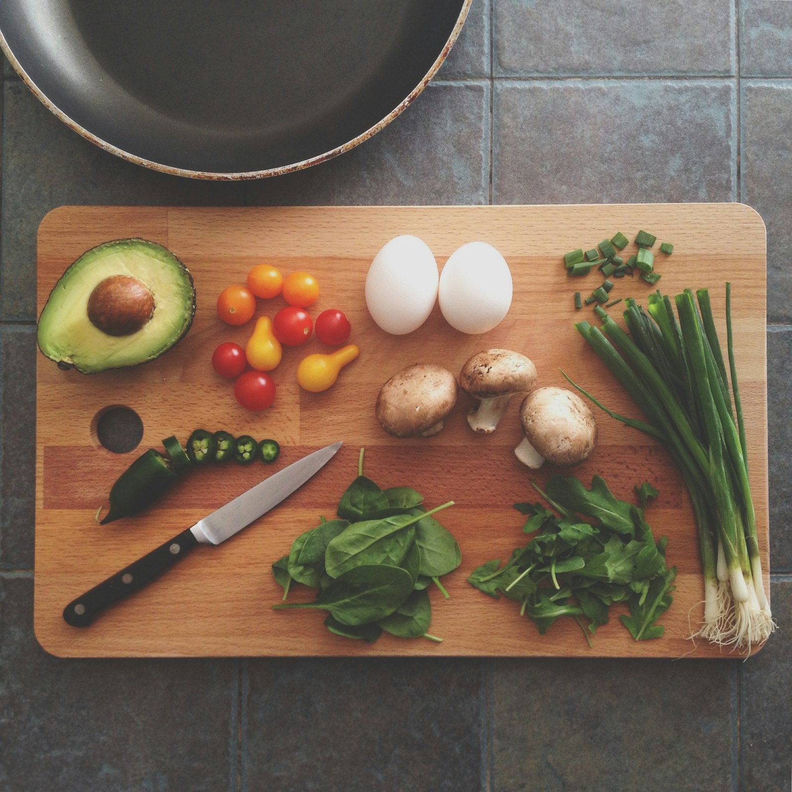 Avocado, tomatoes, eggs, mushrooms and spring onions on a wooden cutting board